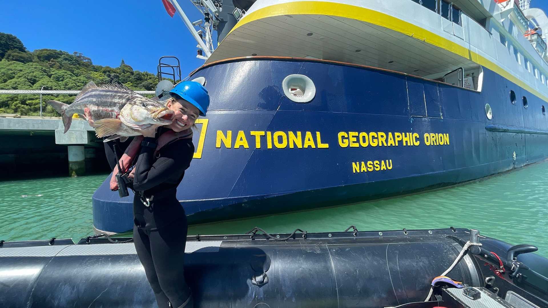 a woman stands in front of a ship holding a large fish