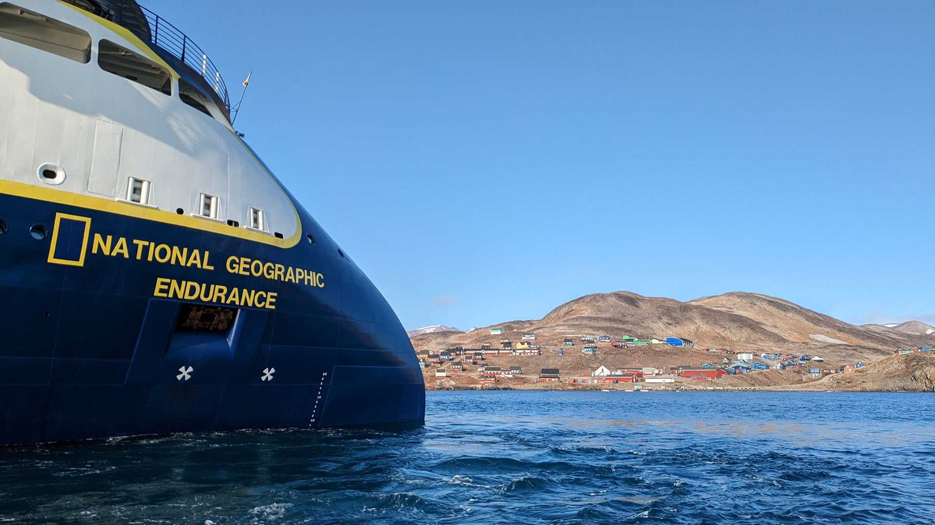 bow of National Geographic Endurance with a colorful Greenlandic village in the background