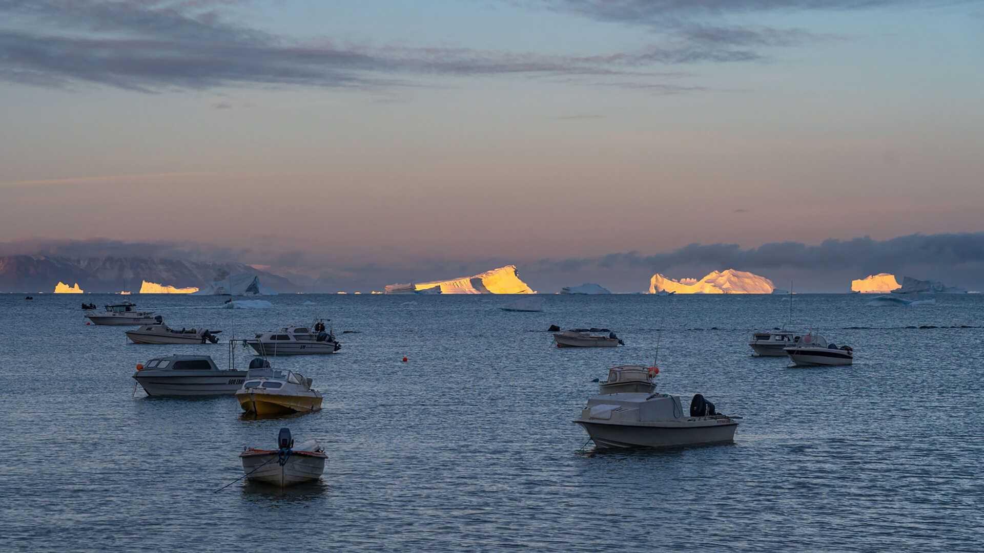 icebergs glowing with boats in the foreground